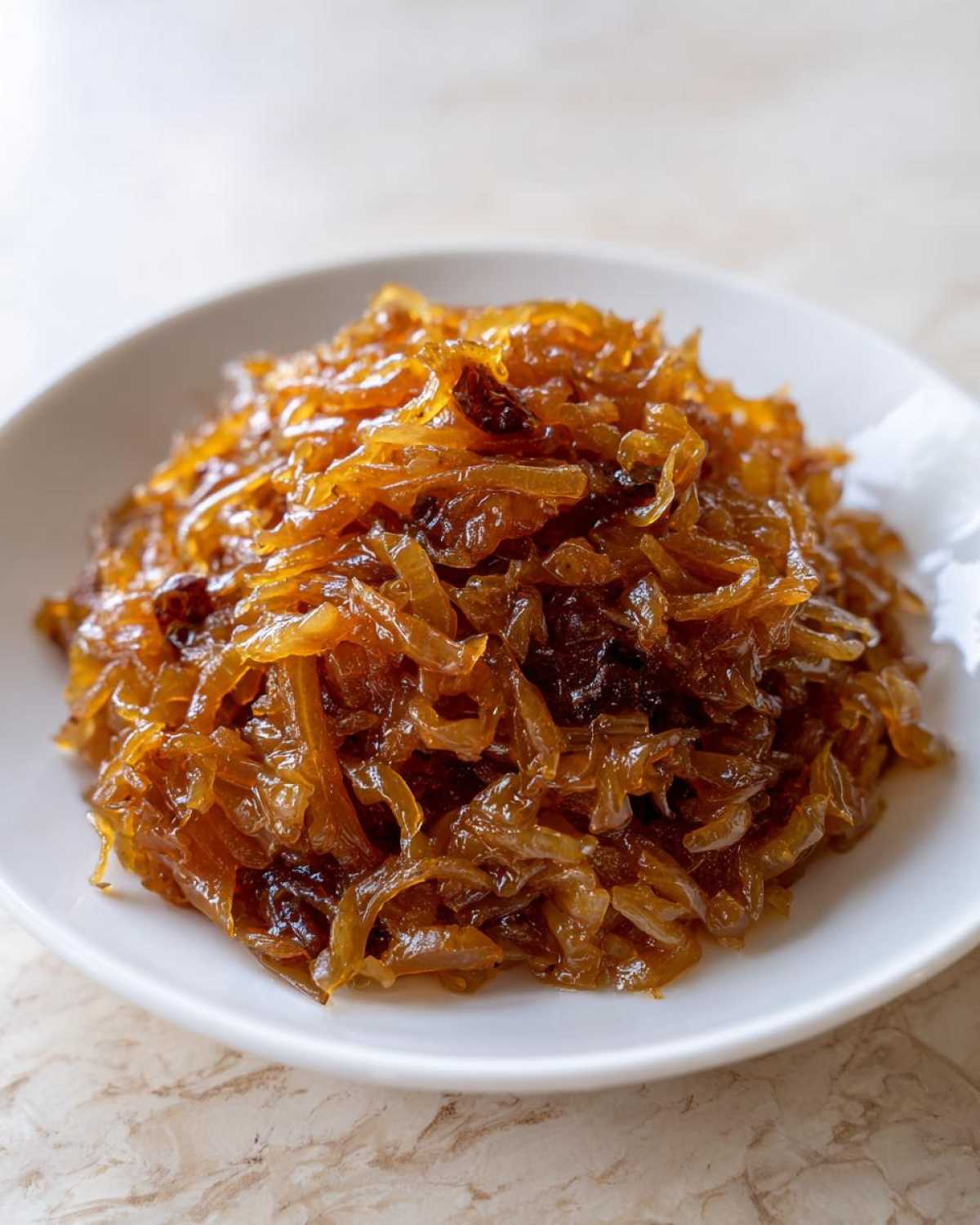 A close-up of a mound of rich, brown caramelized onions served on a small white plate.