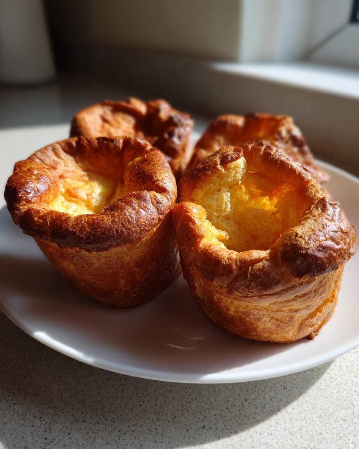 Four golden brown, tall, and perfectly risen yorkshire pudding resting on a white plate.