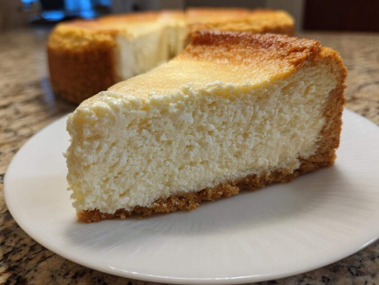 A thick, creamy slice of baked Protein Cheesecake with a golden top and graham cracker crust, served on a white plate.