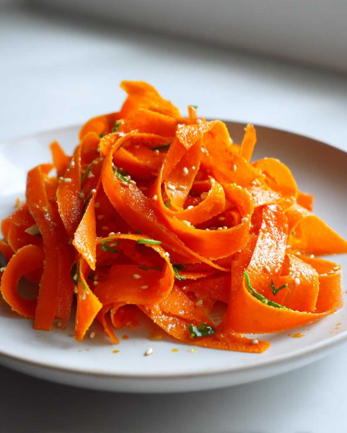 Close-up of vibrant orange ribbon-cut raw carrot salad tossed with sesame seeds and herbs.