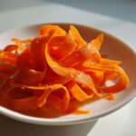 Close-up of vibrant orange ribbons in a raw carrot salad, sprinkled with white sesame seeds.