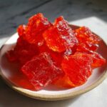 Close-up of vibrant, deep red, jagged pieces of homemade cinnamon rock candy piled on a small, light-colored dish.
