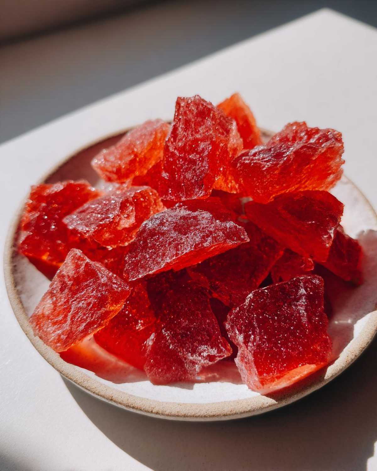 Close-up of bright red, crystalline pieces of homemade cinnamon rock candy served in a small, light-colored bowl.
