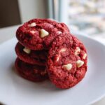 A stack of four vibrant red velvet cake mix cookies studded with white chocolate chips on a white plate.