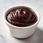 A close-up of thick, glossy homemade chocolate pudding swirled in a small white ramekin.