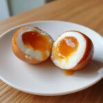 A soft-boiled marinated egg cut in half showing a jammy, runny yolk, perfect for a marinated eggs recipe.