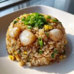 A perfectly molded dome of fried rice topped with seared scallops and fresh green onions, showcasing a delicious seafood variation of fried rice.