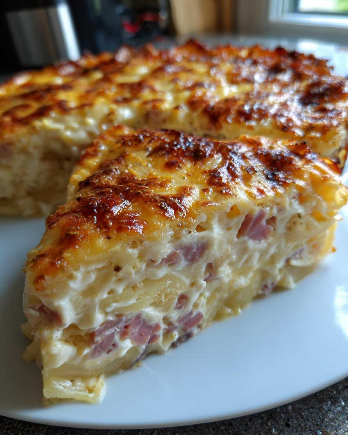 A thick slice of cheesy scalloped potatoes and ham baked in a creamy sauce, showing layers of potato and ham.