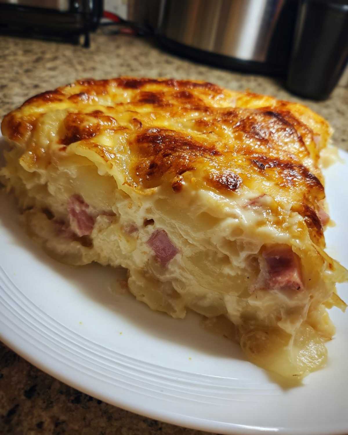 A close-up slice of rich scalloped potatoes and ham with a golden-brown, cheesy crust.