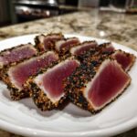 Slices of perfectly seared ahi tuna coated in black and white sesame seeds, showing a rare center.