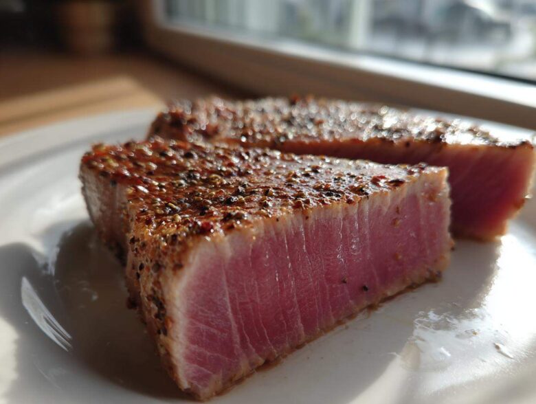 Close-up of two perfectly seared tuna steak portions showing a rare, pink center and a dark, seasoned crust from the MARINADE FOR TUNA STEAK.