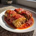 Four homemade cabbage rolls filled with rice and meat, smothered in rich tomato sauce, served on a white plate.