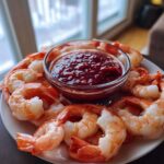 A plate of chilled, cooked shrimp arranged around a small glass bowl of deep red shrimp cocktail sauce.