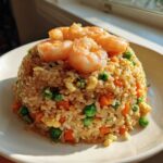 A mound of vibrant shrimp fried rice recipe topped with succulent cooked shrimp, peas, and carrots.