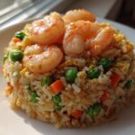 A mound of delicious shrimp fried rice recipe topped with succulent cooked shrimp, peas, and carrots.