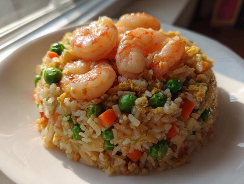 A mound of delicious shrimp fried rice recipe topped with succulent cooked shrimp, peas, and carrots.