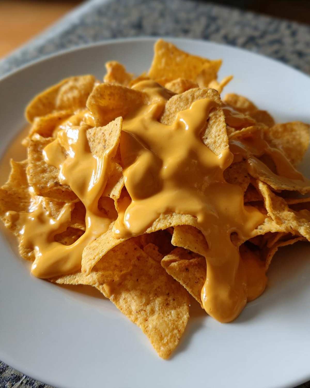 Close-up of tortilla chips smothered in creamy, bright orange nacho cheese sauce.
