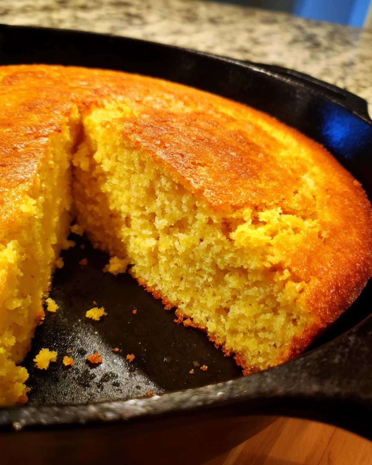 Close-up of a freshly baked, golden-brown skillet cornbread with a slice removed, showing the crumb texture.
