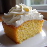 A square slice of yellow cake topped generously with piped swirls of creamy vanilla buttercream frosting.