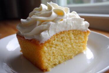 A square slice of yellow cake topped generously with piped swirls of creamy vanilla buttercream frosting.