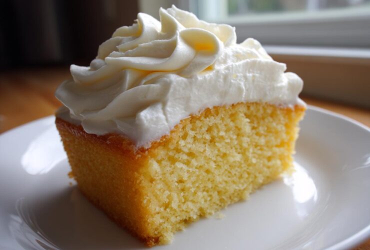 A square slice of yellow cake topped generously with piped swirls of creamy vanilla buttercream frosting.