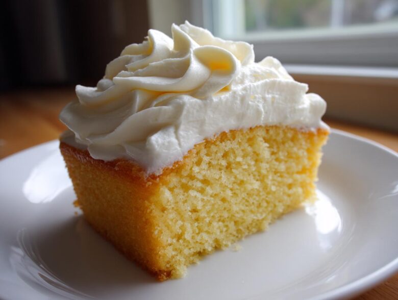 A square slice of yellow cake topped generously with piped swirls of creamy vanilla buttercream frosting.
