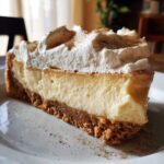 A close-up slice of creamy eggnog cheesecake recipe with a graham cracker crust and whipped cream topping dusted with nutmeg.