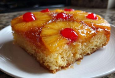 A close-up of a moist slice of pineapple upside down cake topped with caramelized pineapple rings and maraschino cherries.
