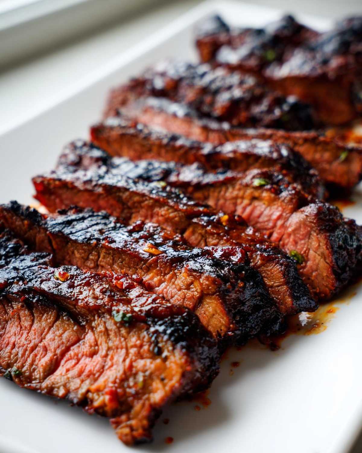 Close-up of perfectly grilled and sliced steak showing a medium-rare center, coated in a rich Carne asada marinade.
