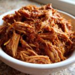 Close-up of a white bowl filled with shredded, saucy Slow Cooker Pulled Pork.