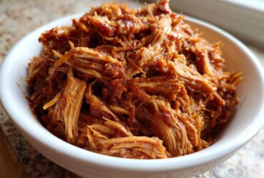 Close-up of a white bowl filled with shredded, saucy Slow Cooker Pulled Pork.