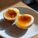 Close-up of two halves of a marinated egg showing a jammy, orange yolk.
