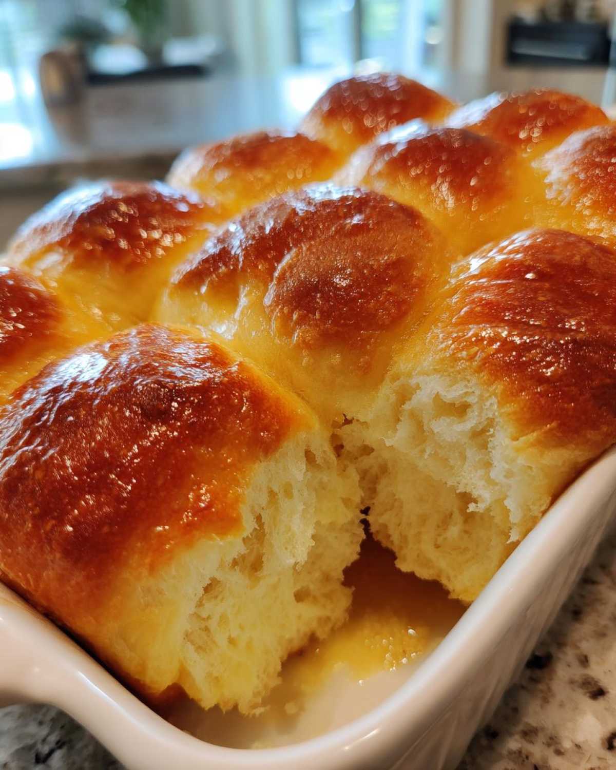 Close-up of golden brown, shiny dinner rolls pulled apart in a white dish, showing soft interior and melted butter.