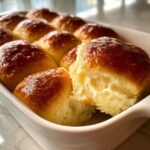 A close-up showing the fluffy interior of one of the soft dinner rolls pulled apart in a white baking dish.