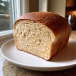 A close-up of a freshly baked loaf of whole wheat bread, sliced to show its soft, even crumb.