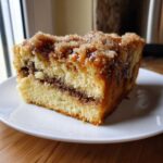 A close-up of a moist slice of sour cream coffee cake featuring a rich cinnamon swirl and sugary streusel topping.
