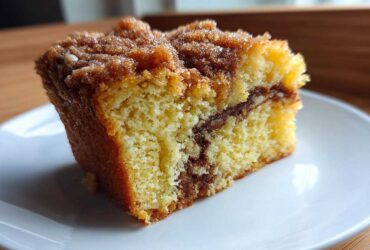 Close-up of a moist slice of sour cream coffee cake showing a yellow crumb and cinnamon swirl topping.