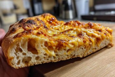 Close-up of a slice of pizza showing the airy crumb structure made from sourdough discard pizza dough.