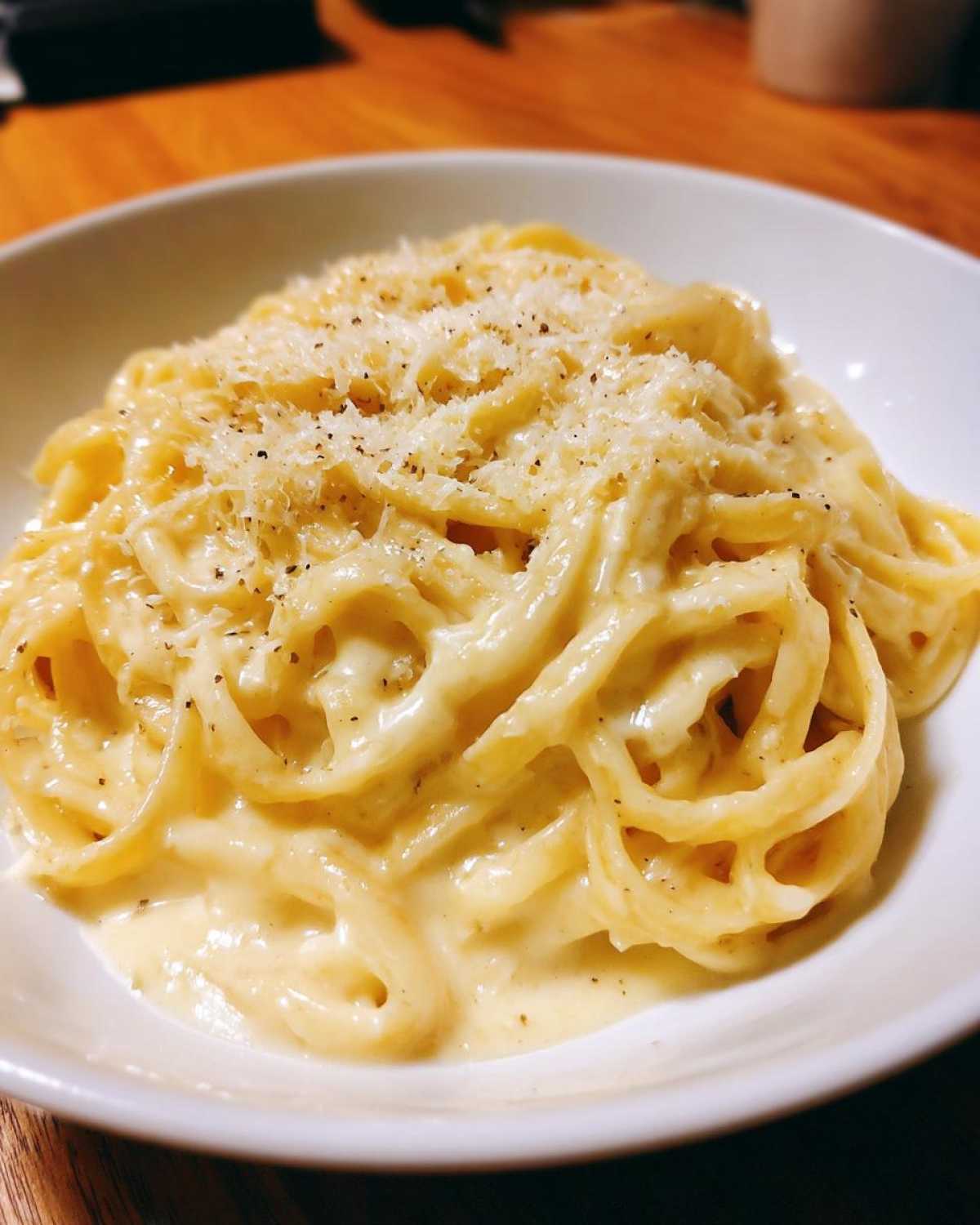 Close-up of spaghetti generously coated in rich, creamy homemade alfredo sauce and topped with grated cheese and black pepper.