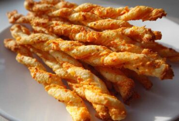 A close-up of a stack of golden, twisted, spicy Southern cheese straws resting on a white plate.