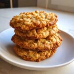 A stack of four chewy, golden brown oatmeal cookie treats on a white plate.