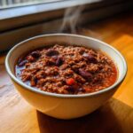 A steaming bowl of rich, hearty chili loaded with ground meat and kidney beans, showcasing the best chili recipe.