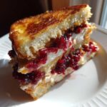A cross-section of stuffed french toast filled with cream cheese and bright red berry jam.