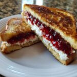 Close-up of stuffed french toast cut in half, showing creamy filling and bright red jam.