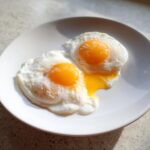 Two sunny-side up eggs with bright orange yolks served on a white plate, illustrating perfect poached eggs technique.