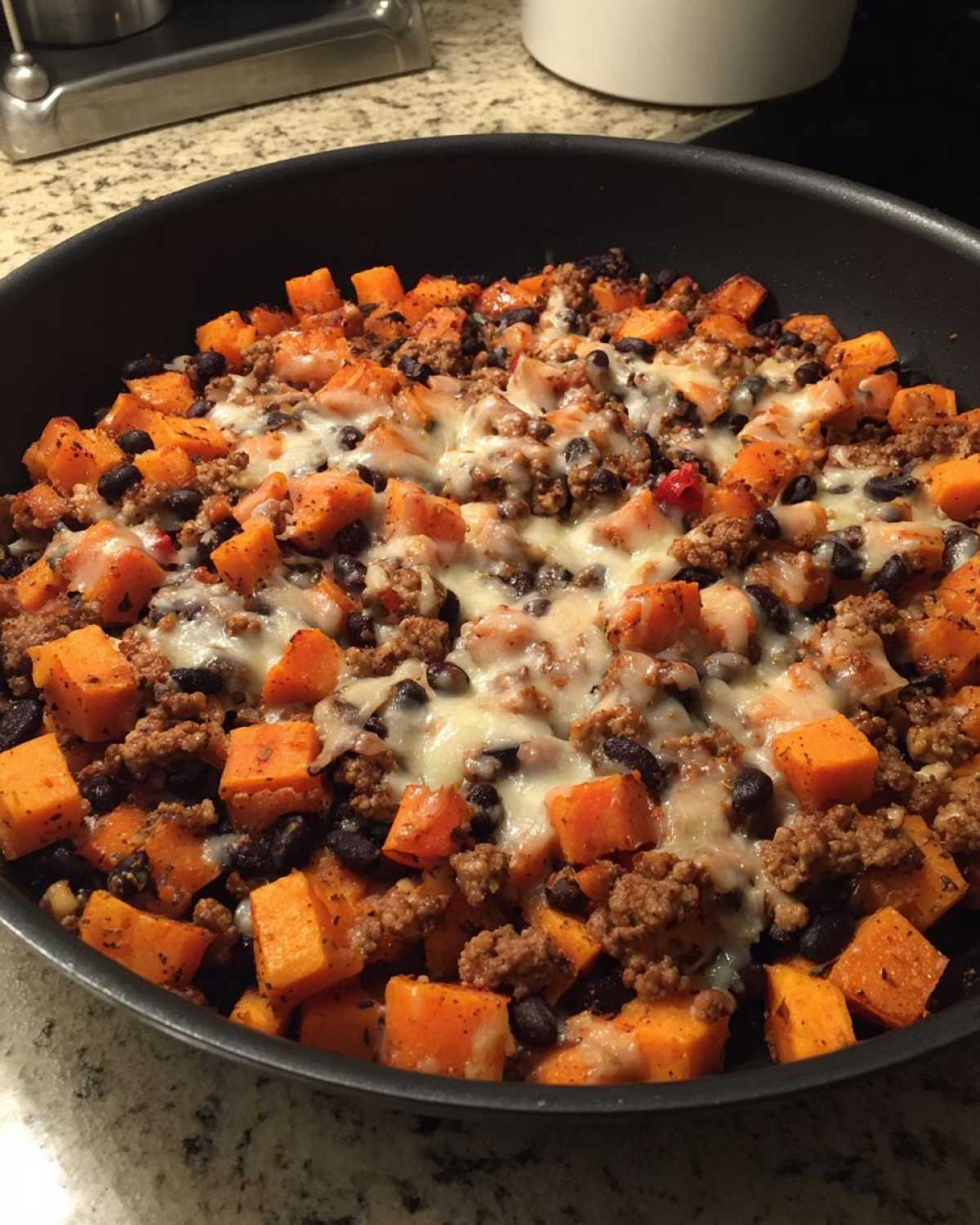 Close-up of a sweet potato skillet with diced sweet potatoes, ground meat, black beans, and melted cheese.