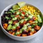 Close-up of a vibrant sweet potato taco bowl featuring roasted sweet potatoes, black beans, corn, and a generous drizzle of green avocado sauce.