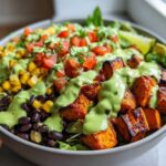 Close-up of a vibrant sweet potato taco bowl featuring roasted sweet potatoes, black beans, corn, pico de gallo, and a creamy green avocado dressing.
