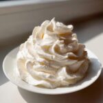 A perfect swirl of thick, white cream cheese frosting piped onto a small white plate.