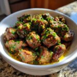 Close-up of tender crockpot steak bites coated in garlic butter and fresh parsley.